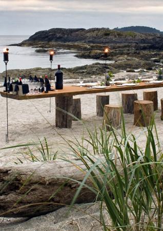A table with candles and wooden stools on a beach at sunset.